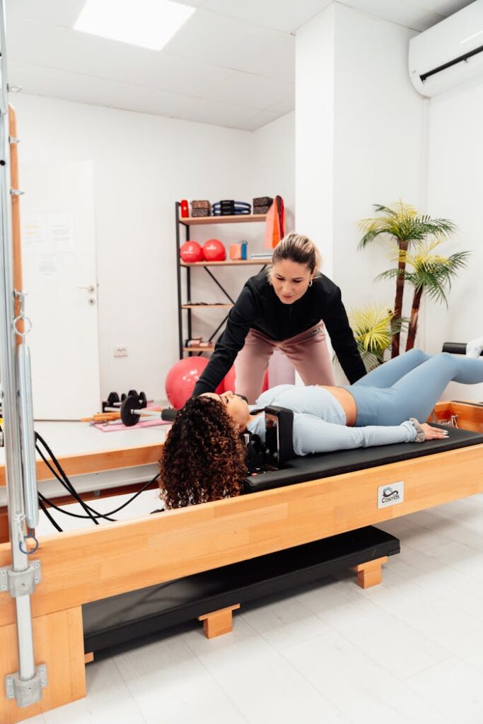 Two women practicing Pilates on reformer machine in a well-equipped gym.