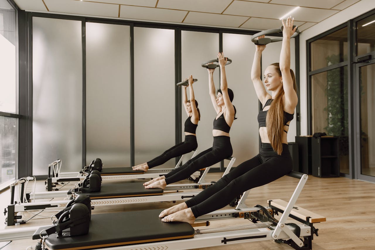 Three women synchronously practicing Pilates on reformers in a modern gym studio.